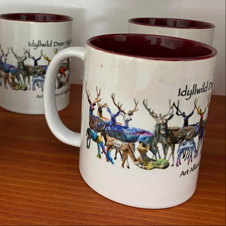 Set of mugs with deer illustrations and 'Idyllwild Deer Sighting' text on a wooden surface.