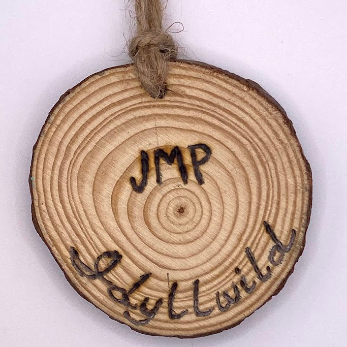 Wooden circular ornament with 'JMP Wild' engraving on a white background