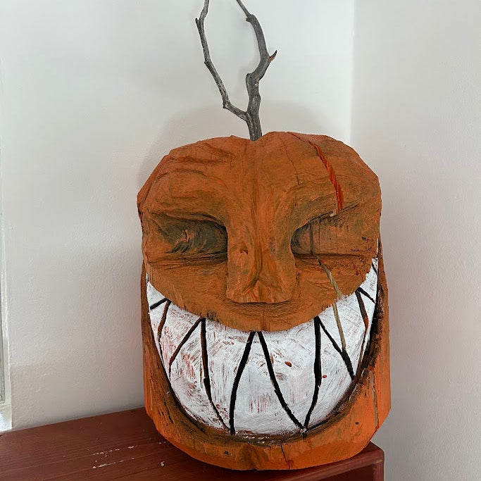 Wooden jack-o-lantern pumpkin with white teeth and black details on a wooden surface.