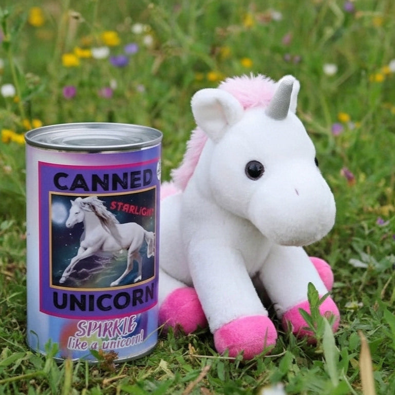 Plush unicorn toy next to a can labeled 'Canned Unicorn' in a grassy field with flowers