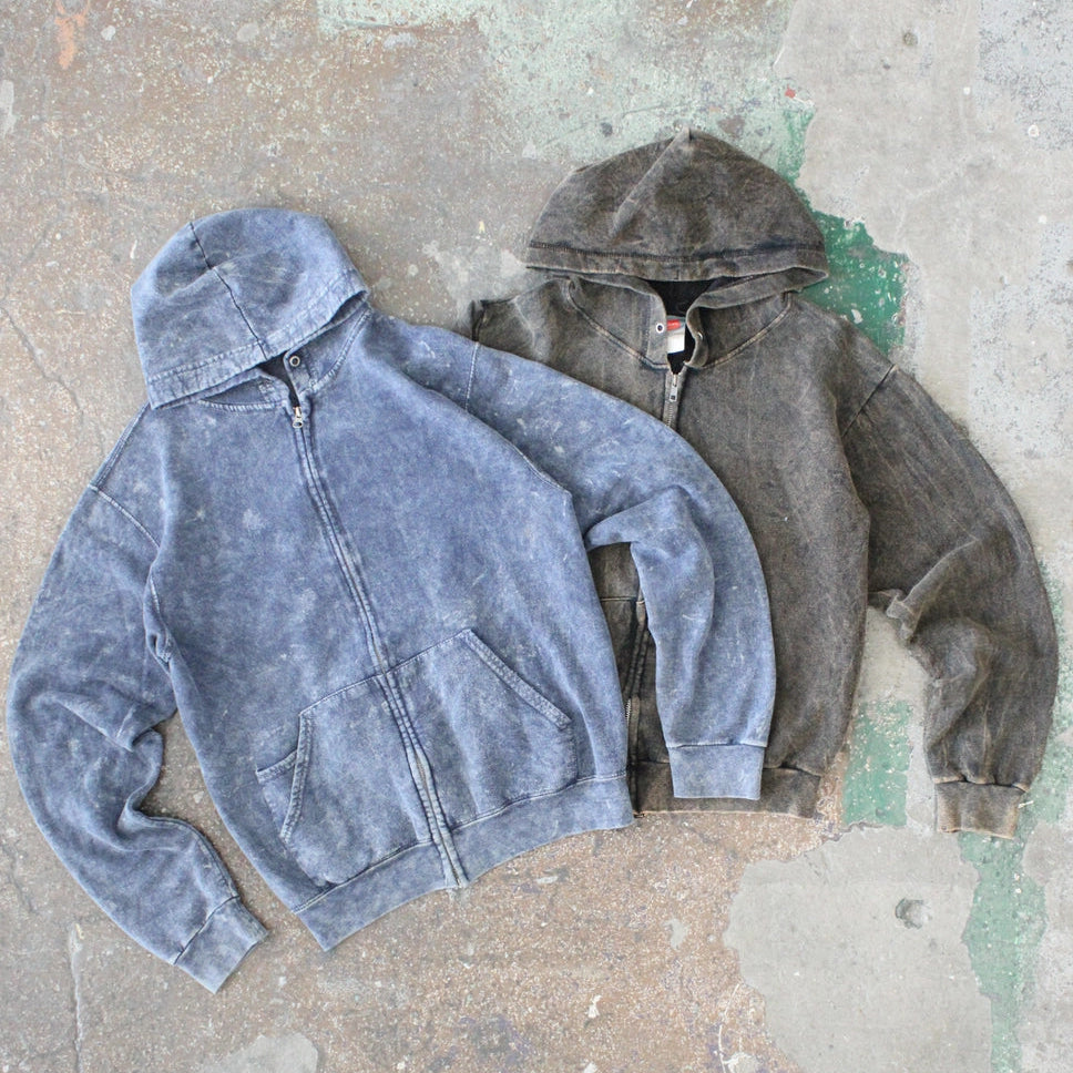 Two hoodies, one blue and one gray, on a textured surface.