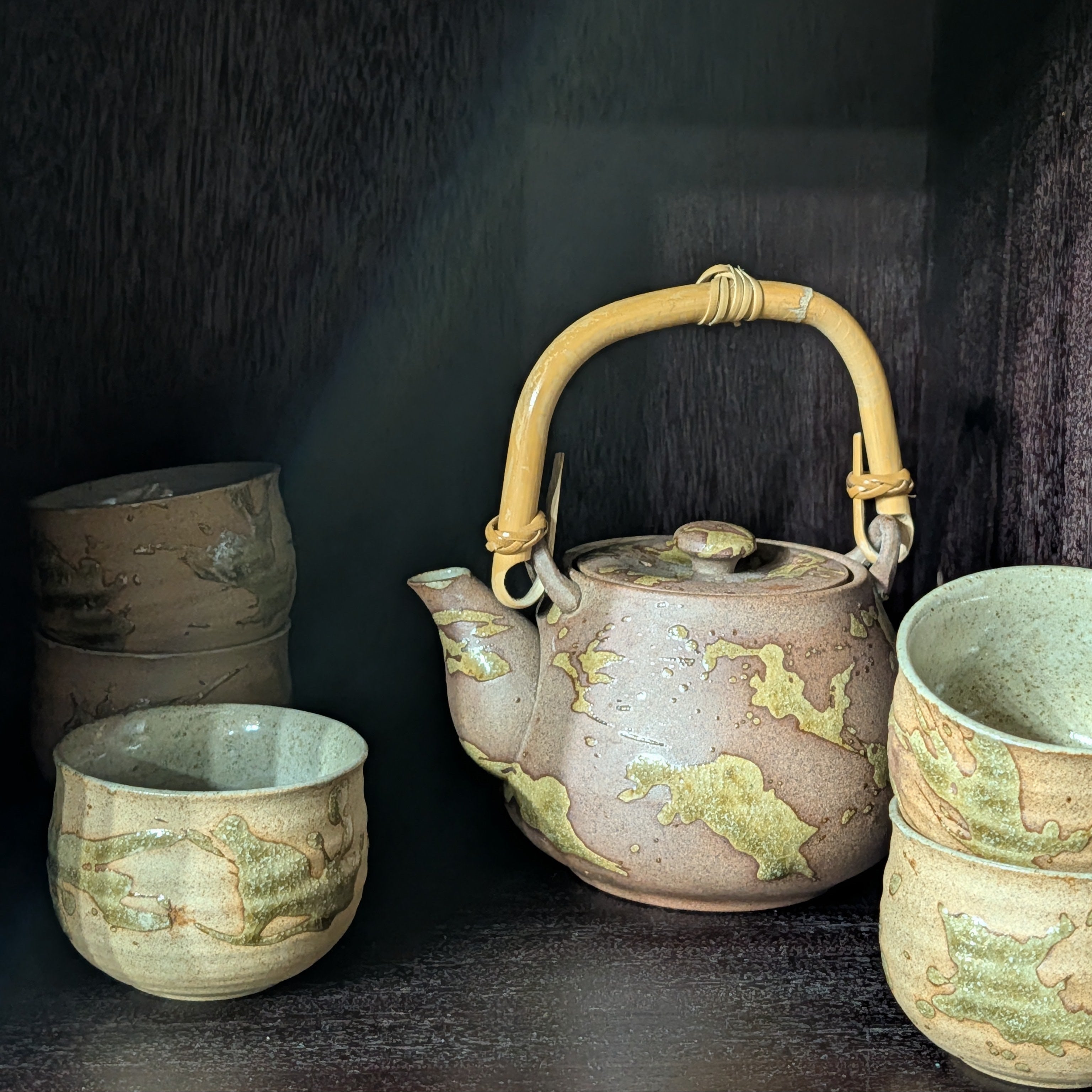 Set of ceramic teapots with decorative handles and patterns on a dark background