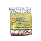 A packaged food product wrapped in a floral patterned cloth and tied with a textured olive-green paper band featuring a gold wax seal, shown on a plain white background.
