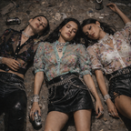 Three women lying on the ground with drinks, wearing stylish outfits.