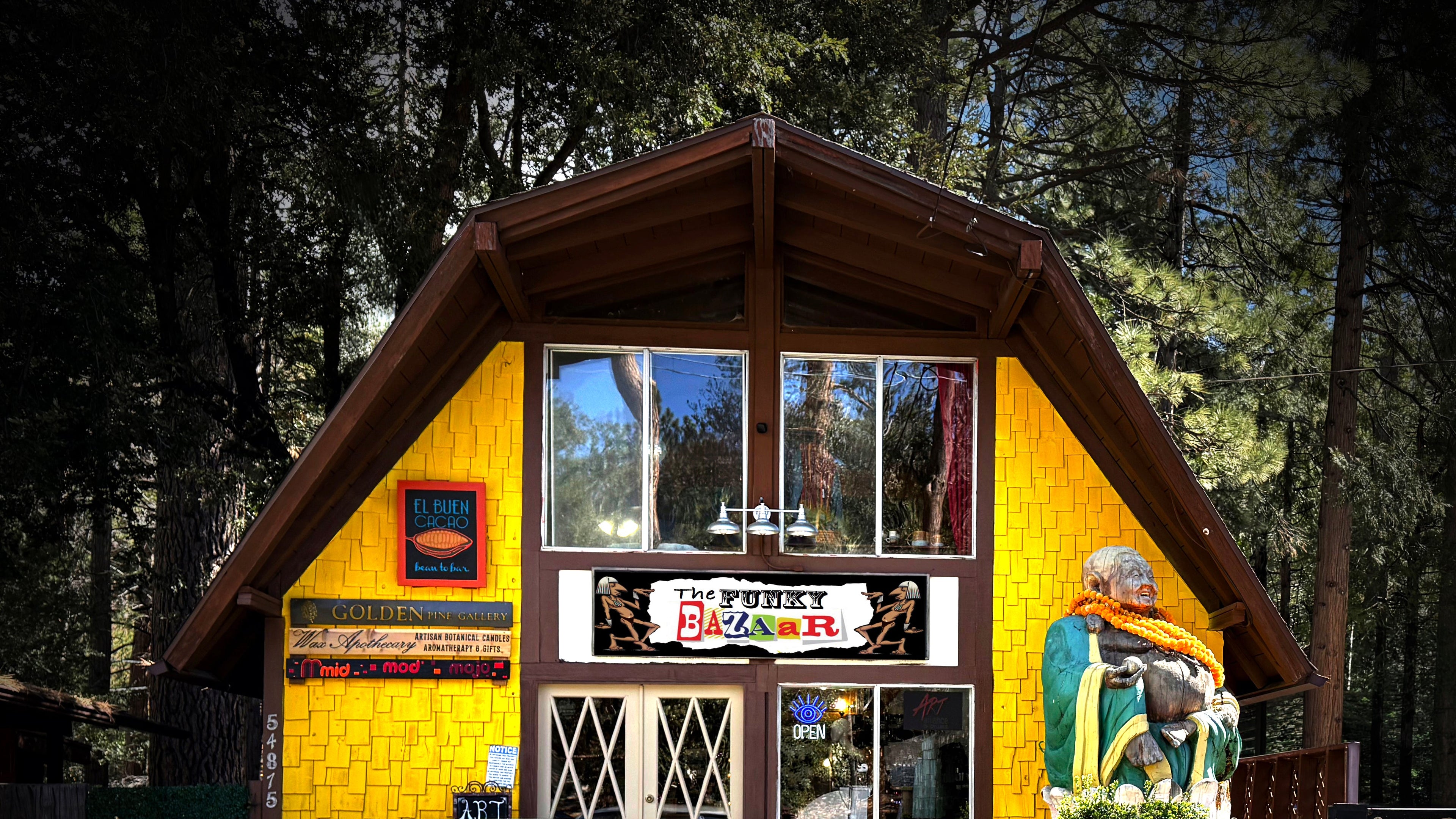 Vintage car parked in front of The Funky Bazaar of Idyllwild, a unique yellow building with a Buddha statue.