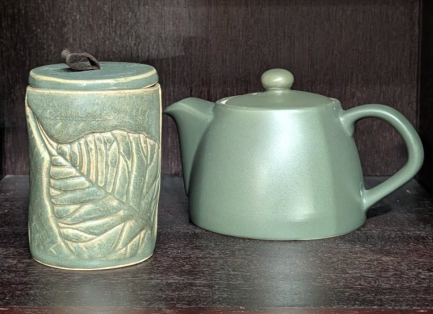Two ceramic pieces, a jar and a teapot, on a dark surface with a dark background.