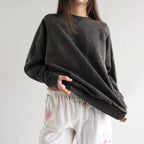 Person wearing a dark gray oversized sweater with white pants featuring floral embroidery on a plain background
