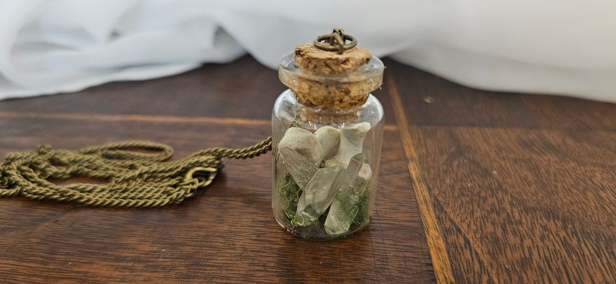 Handcrafted miniature glass vial pendant necklace filled with real preserved bone fragments, clear quartz crystal points, and green moss with an antique bronze chain.