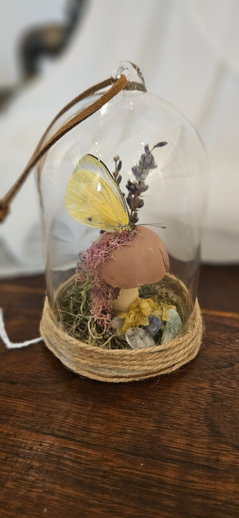 alt="Handcrafted glass cloche terrarium display with a preserved yellow butterfly on a sculpted mushroom, dried lavender, moss, and crystal chips bound in jute twine"