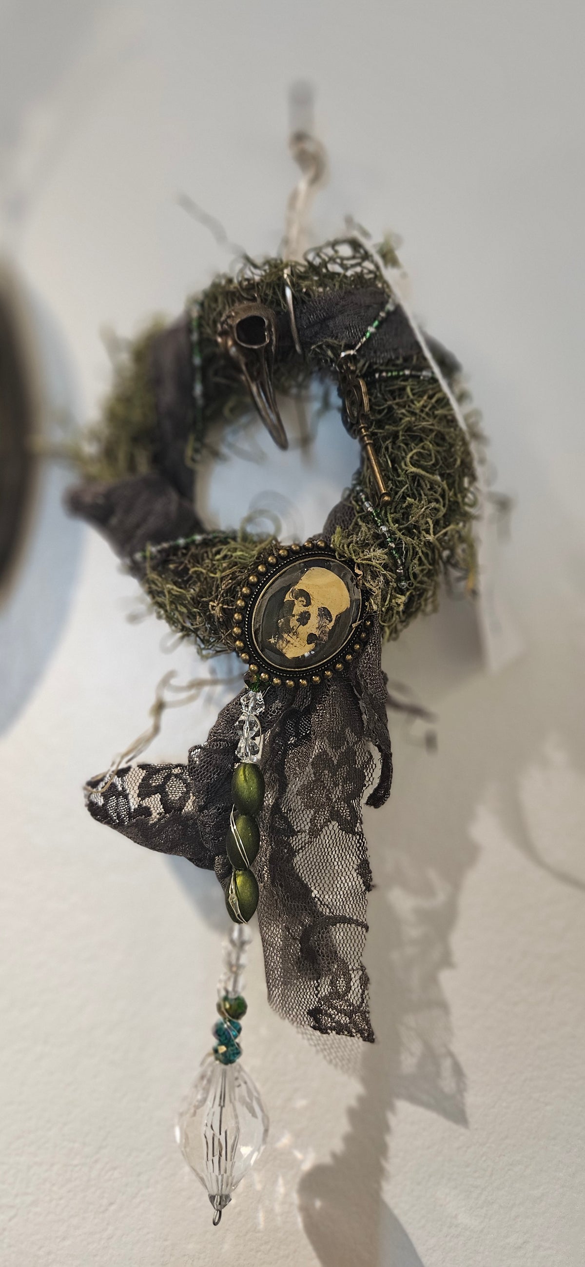 Handcrafted gothic mini moss wreath decorated with a skull cameo pendant, bird skull charm, antique key, black lace ribbon, and a hanging crystal drop.