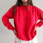 Person wearing a red sweater and white pants with floral patterns against a plain background