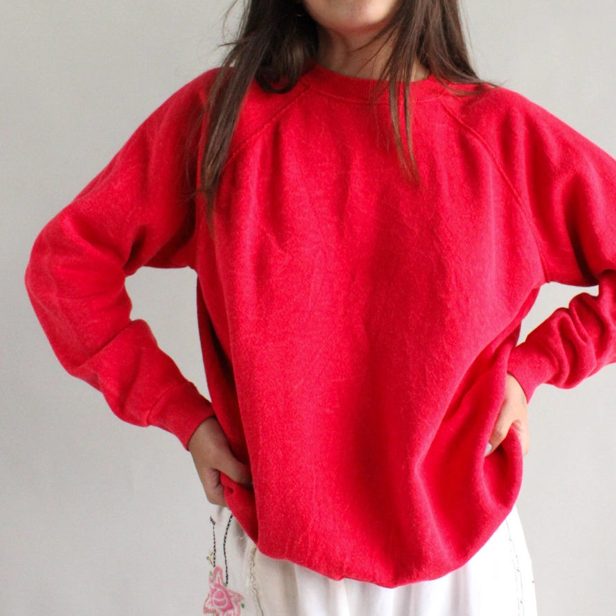 Person wearing a red sweater and white pants with floral patterns against a plain background