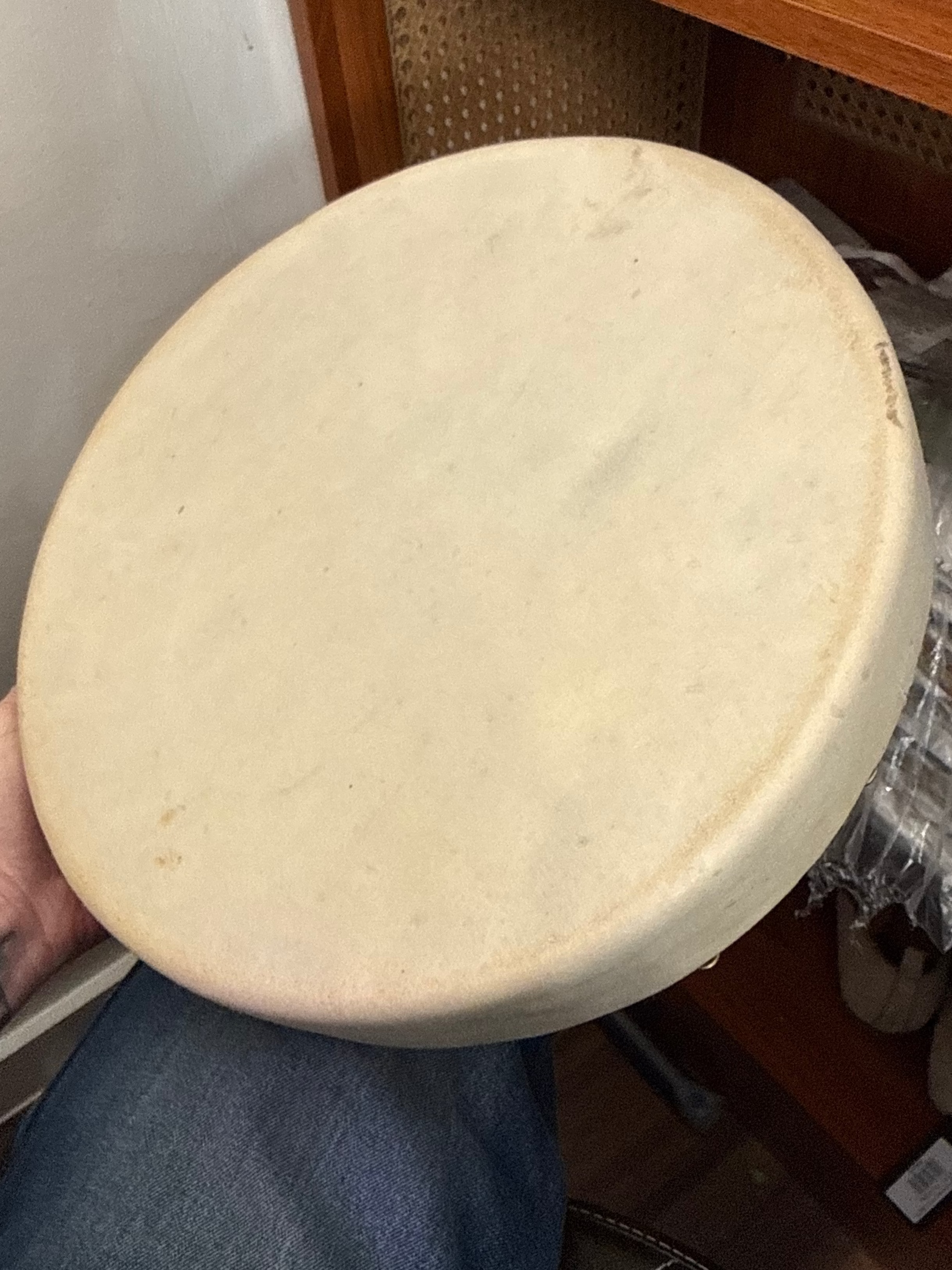An angled top view of a round Lakota rawhide hand drum showing the smooth, light beige drumhead surface and the thick rim wrapped in natural hide.