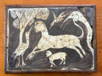 A rectangular 10th to 12th century Persian sgraffito ceramic tile fragment featuring an incised cream-colored rearing lion or mythical beast against a dark slip background, surrounded by stylized birds and a textured tree canopy, showcased in a simple wooden frame.