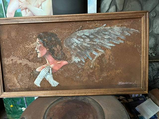 A framed horizontal mixed media painting,  depicting the side profile of a winged angel or opera singer with long dark hair, wearing long white opera gloves and looking to the left. The background features a heavily textured, sandy brown surface resembling rusted metal, and the right side displays a textured, light gray wing extending outward within a simple wooden frame.