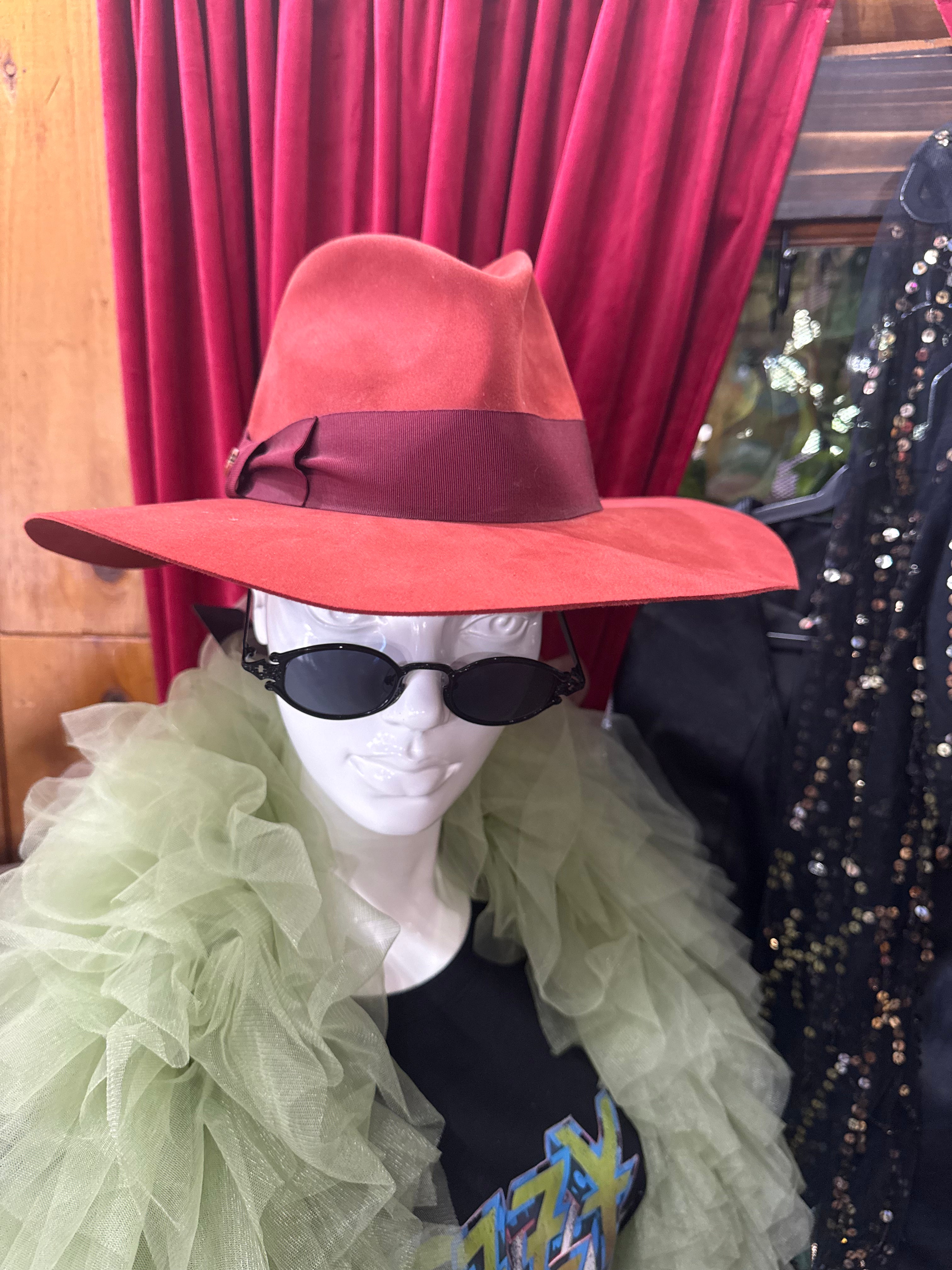 A vibrant terracotta red Loro Piana velvet felt fedora hat featuring a classic creased crown and a wide brim, accented with a dark burgundy grosgrain ribbon band.