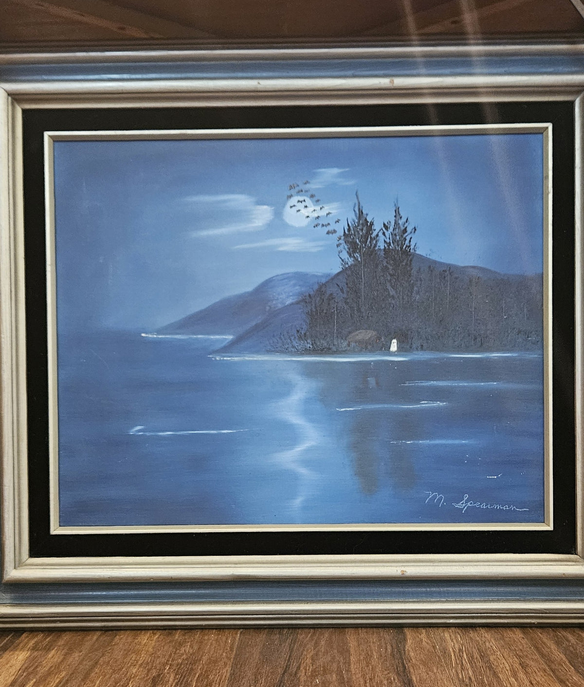 Original nocturnal oil painting of a blue moonlit lake and forested island shore with a small ghost standing by the water, signed M. Spearman in a layered vintage frame.
