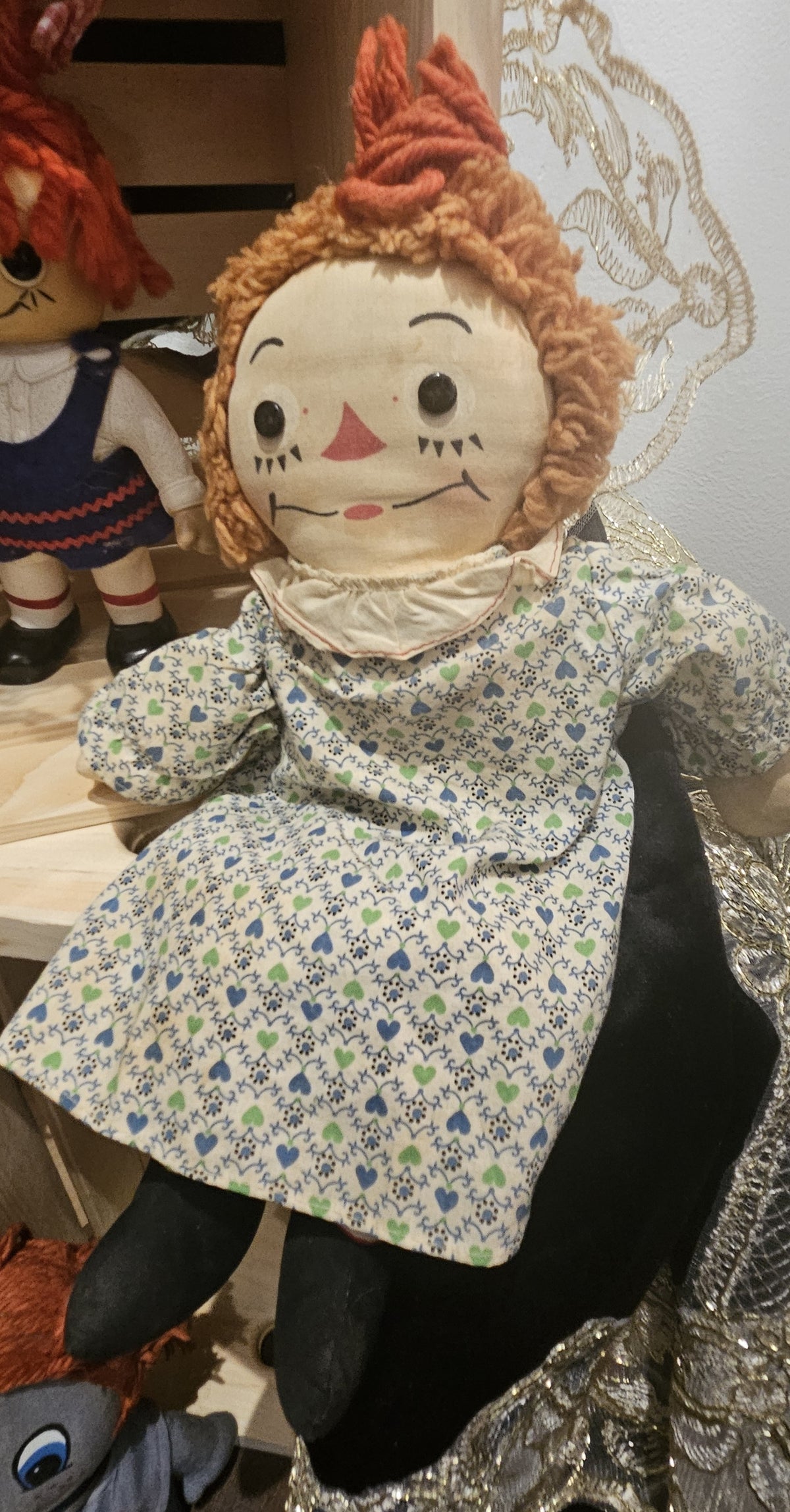 "Classic vintage Raggedy Ann doll with orange yarn hair and a hand-painted face, wearing a blue and green heart patterned dress with a white collar."